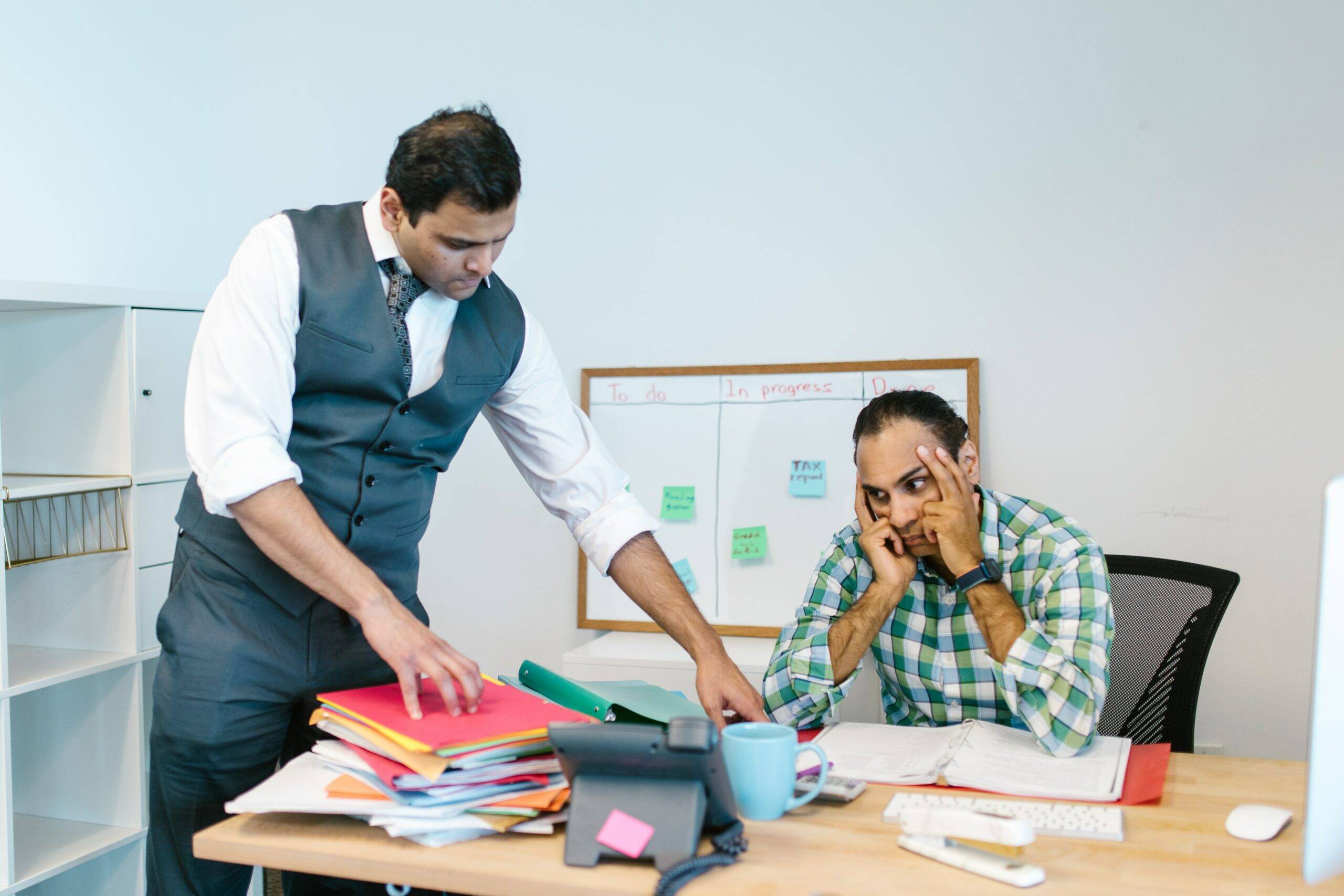 Two Indian office workers, male looking at files, one frustrated
